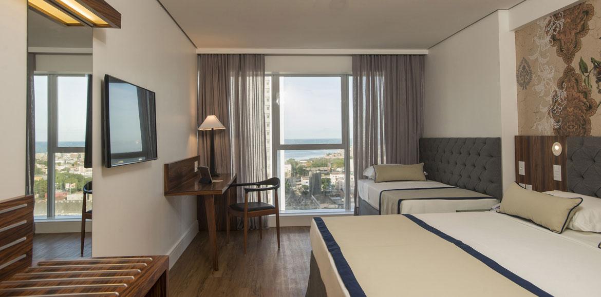 Hotel Luzeiros Recife Bagian luar foto The photo shows a modern hotel room. It features two beds with a simple design, one larger and one smaller. There's a large window with sheer curtains, allowing natural light to fill the space and offering a view of the outside. A wooden desk and cha