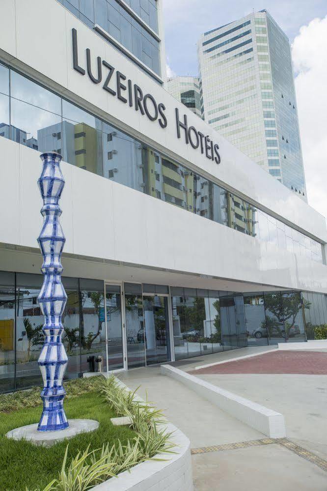 Hotel Luzeiros Recife Bagian luar foto The photo shows a modern hotel building with large glass windows and a sleek, white facade. In front of the hotel, there is a tall, decorative sculpture that features a unique, twisting shape with a blue and white color scheme. The hotel name is prom